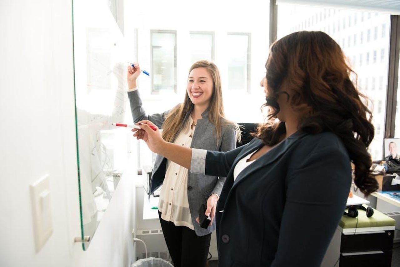 Un_datore_di_lavoro_affidabile_e_attraente_3FmFavCiAX - Veicoli24 Source: Christina Morillo - pexels - Two professional women discussing ideas on a whiteboard in a modern office setting.