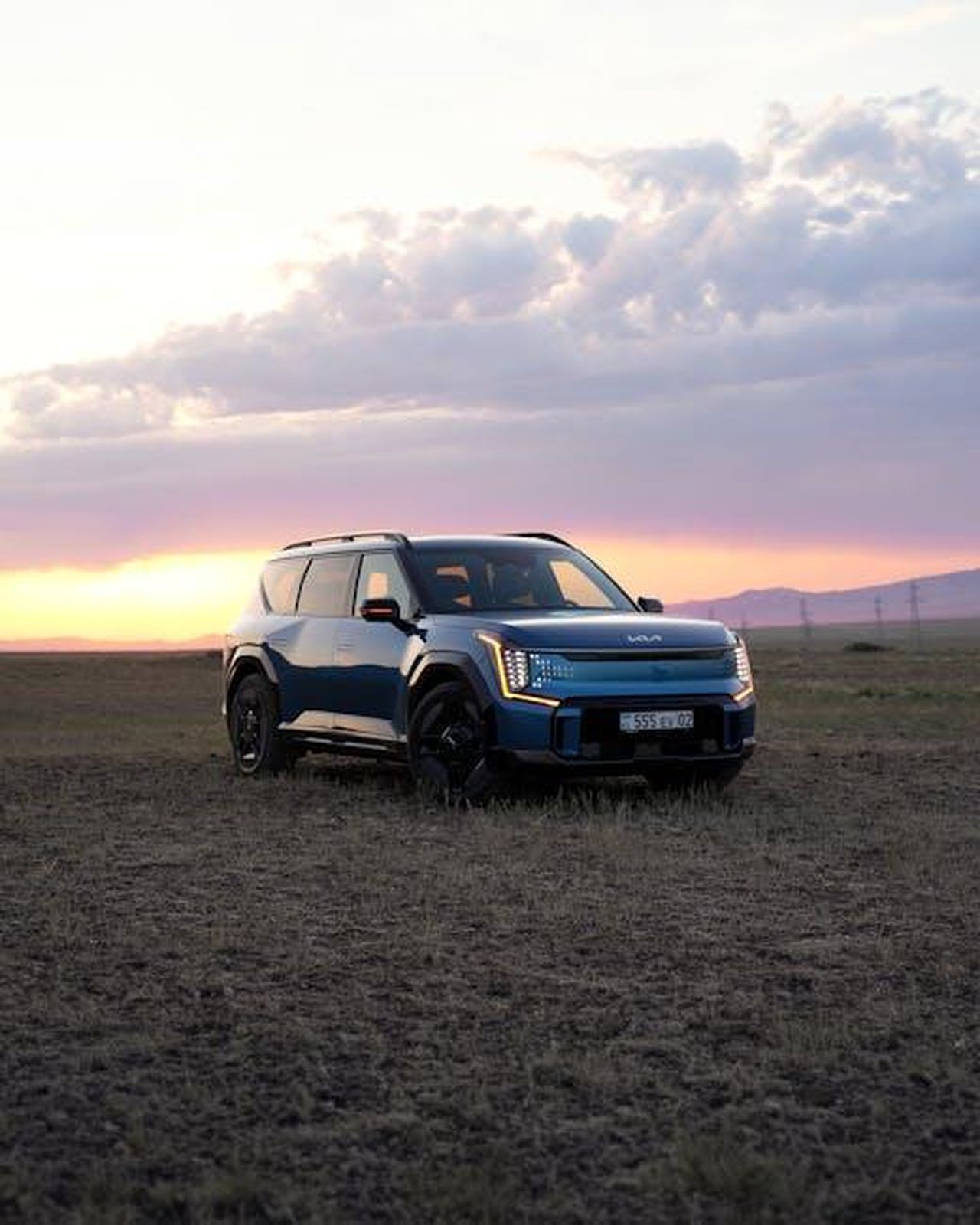 Iniziative_e_investimenti_di_Kia_Q9C5dCFBNa - Veicoli24 Source: Hyundai Motor Group - pexels - A blue electric SUV parked in a grassy field during sunset with dramatic sky and canyon backdrop.