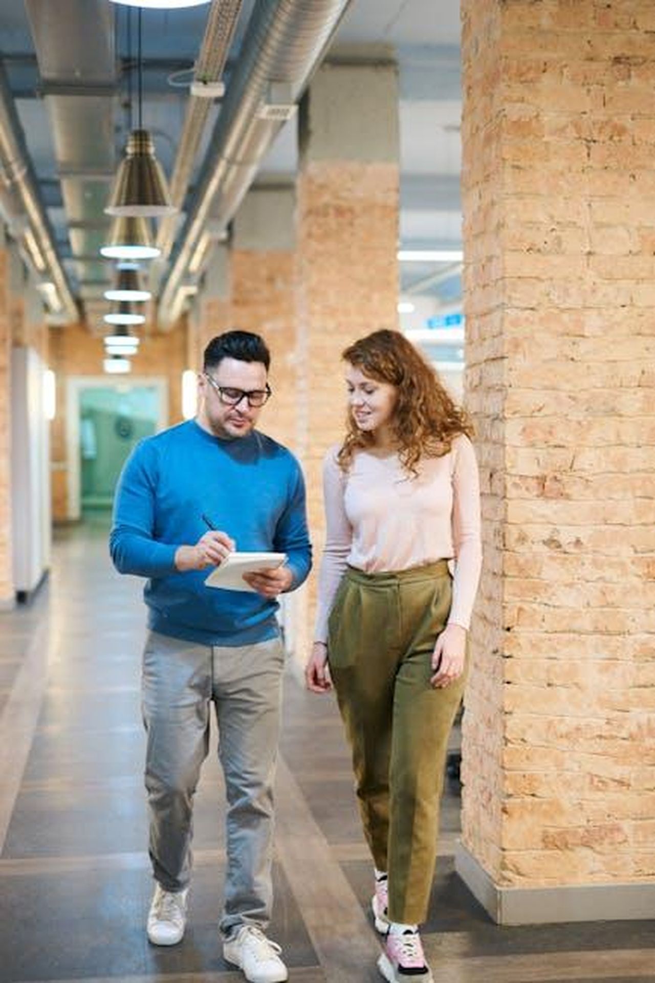 Processo_di_selezione_degli_studenti_H5GaIAYQVj - Veicoli24 Source: fauxels - pexels - Two business colleagues walking in an office hallway discussing ideas with a notepad.