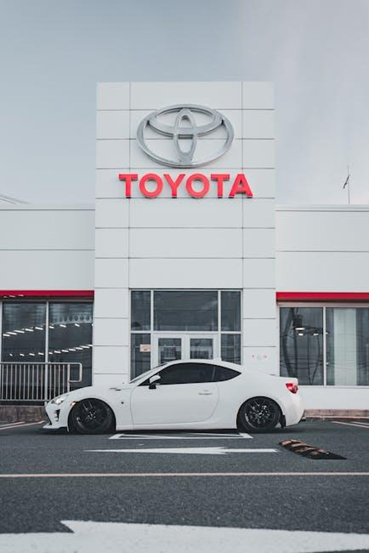 Risultati_di_vendita_di_marzo_2025_DnBaWrJpjC - Veicoli24 Source: Erik Mclean - pexels - Sleek white car parked in front of a Toyota dealership showcasing modern automotive design.