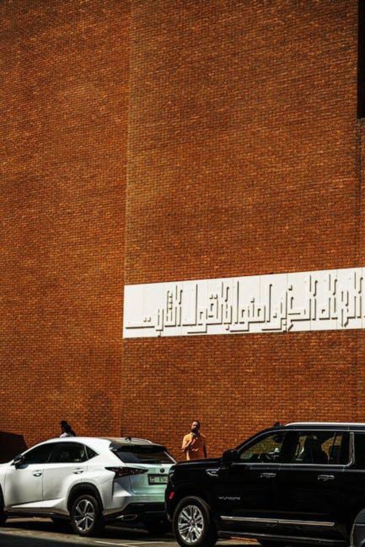 Suddivisione_dei_Gradi_XffZtVWqCo - Veicoli24 Source: aboodi vesakaran - pexels - Street view of a brick building in Dubai with parked cars and a person walking.